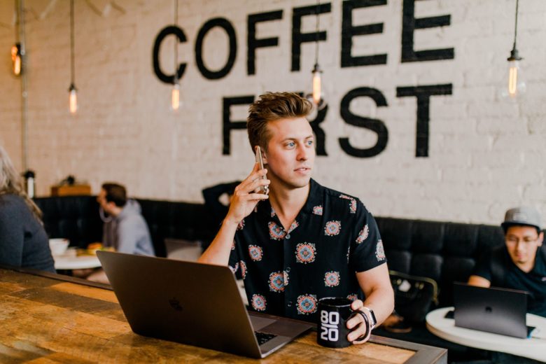 A person using phone to call while using laptop in a coffee shop